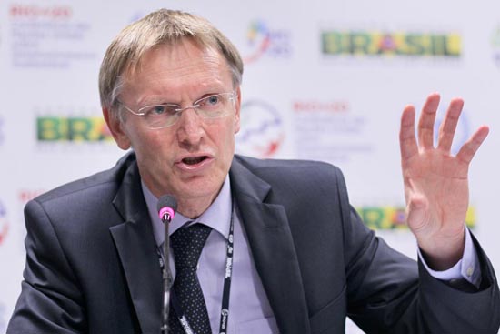 Palestrante formal discursando em evento oficial com o banner 'BRASIL' ao fundo, destacando temas nacionais e institucionais.