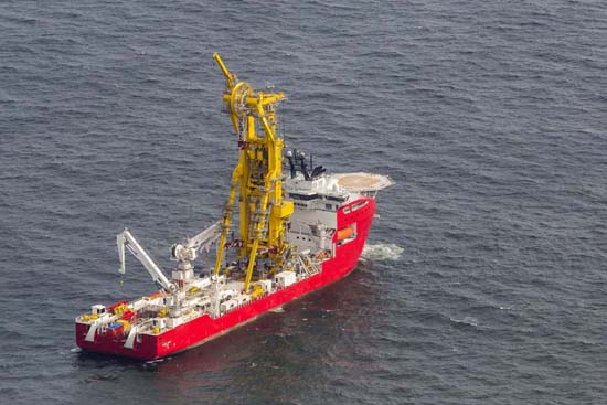 Navio de instalação de tubos offshore, com estrutura amarela para colocação de tubos no fundo do mar, heliponto na popa e diversos guindastes no convés.
