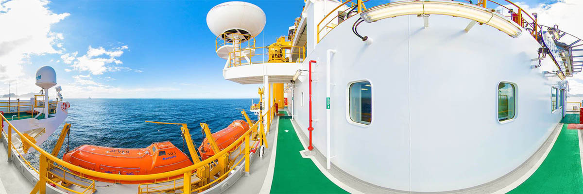 Vista de uma plataforma offshore com botes salva-vidas laranja, radar esférico branco e passarela verde, destacando medidas de segurança marítima.