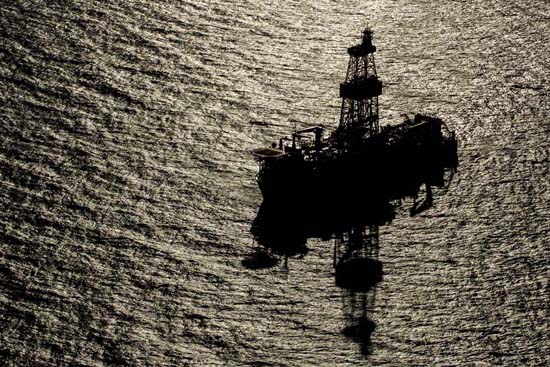 Plataforma de petróleo offshore, navio sonda, NS-45, com estrutura destacada ao pôr do sol, refletindo na superfície do oceano e destacando a grandiosidade da extração marítima.