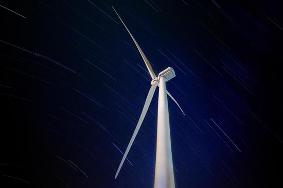 Turbina eólica contra um céu noturno estrelado, simbolizando a integração da energia renovável com o meio ambiente e a beleza natural do universo.